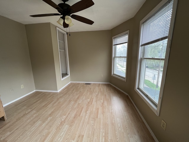 unfurnished room with a ceiling fan, visible vents, light wood-style floors, and baseboards