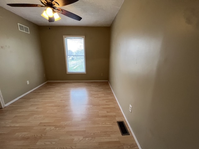 spare room with baseboards, a ceiling fan, visible vents, and light wood-type flooring