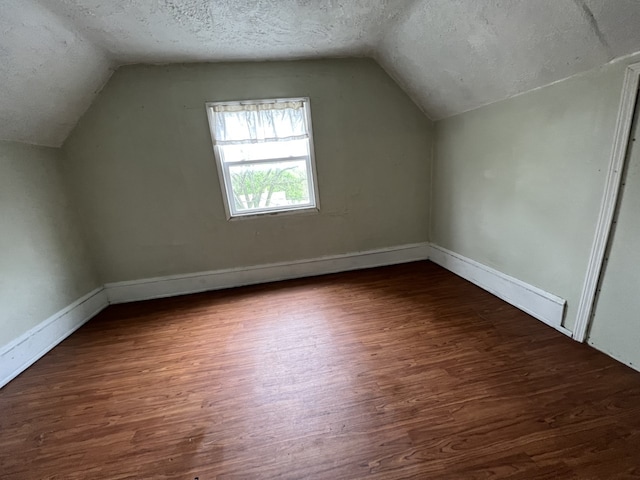 additional living space featuring vaulted ceiling, a textured ceiling, baseboards, and wood finished floors