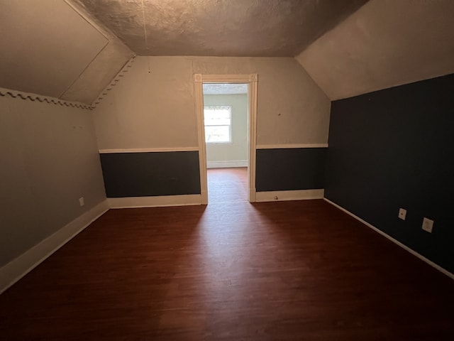 bonus room with dark wood-type flooring, baseboards, lofted ceiling, and a textured ceiling