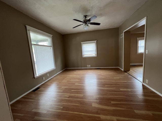 spare room with ceiling fan, a textured ceiling, baseboards, and wood finished floors