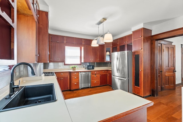 kitchen featuring wood finished floors, a sink, hanging light fixtures, light countertops, and appliances with stainless steel finishes