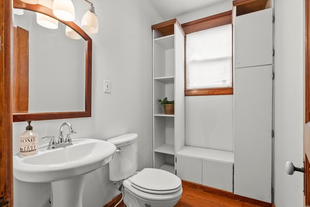 half bath with toilet, wood finished floors, and a sink