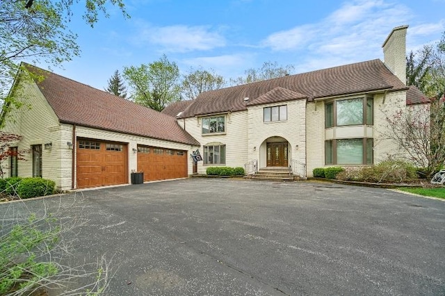 view of front of home featuring brick siding, central AC unit, driveway, and a chimney