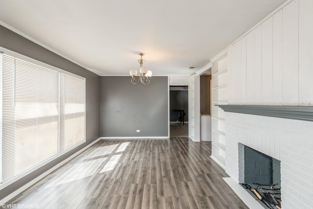 unfurnished living room featuring ornamental molding, wood finished floors, an inviting chandelier, baseboards, and a brick fireplace