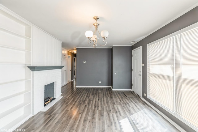 unfurnished living room featuring wood finished floors, an inviting chandelier, a fireplace, crown molding, and baseboards