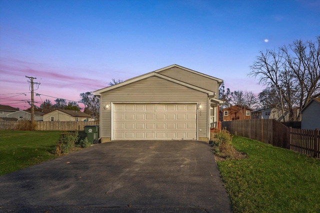 garage at dusk featuring a yard, driveway, and fence