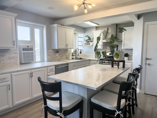 kitchen featuring a sink, light wood-type flooring, a kitchen bar, white cabinets, and stainless steel dishwasher