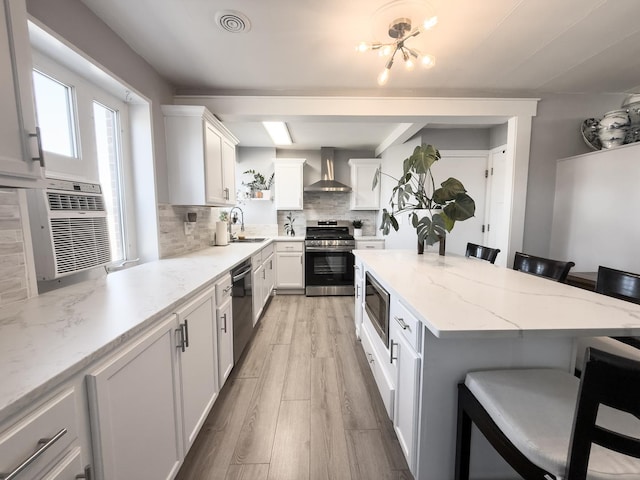 kitchen featuring visible vents, a breakfast bar area, appliances with stainless steel finishes, wall chimney exhaust hood, and a sink