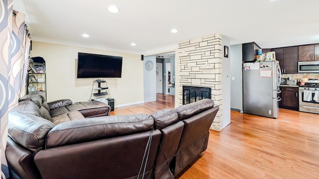 living room featuring recessed lighting, a stone fireplace, light wood-style flooring, and ornamental molding