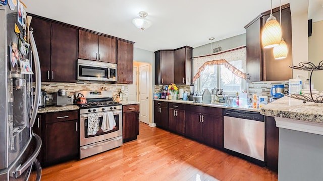 kitchen featuring a sink, stainless steel appliances, dark brown cabinets, light wood-type flooring, and backsplash