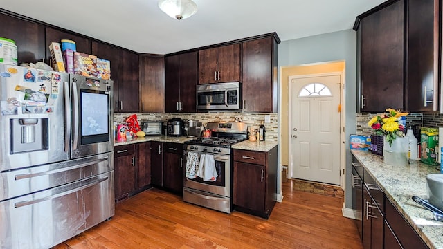 kitchen with dark brown cabinets, light stone countertops, appliances with stainless steel finishes, and wood finished floors