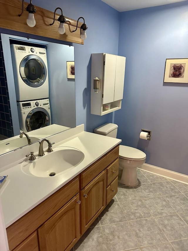 bathroom featuring baseboards, toilet, stacked washer and clothes dryer, tile patterned floors, and vanity