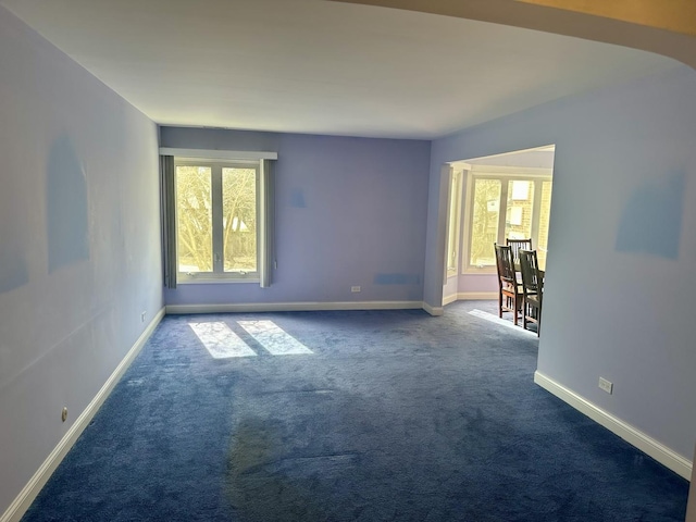 unfurnished room featuring a healthy amount of sunlight, baseboards, and dark carpet