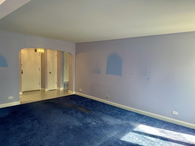 empty room featuring baseboards, arched walkways, carpet flooring, and tile patterned flooring