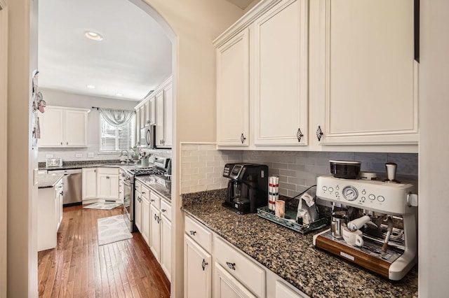 kitchen featuring dark wood-style floors, arched walkways, decorative backsplash, white cabinets, and appliances with stainless steel finishes