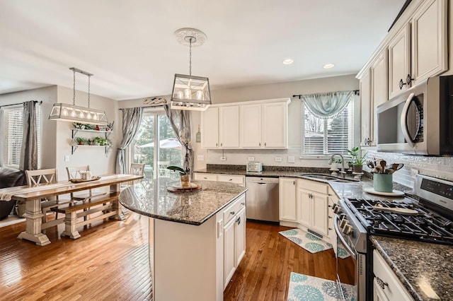 kitchen featuring a sink, a kitchen island, hardwood / wood-style floors, stainless steel appliances, and dark stone counters