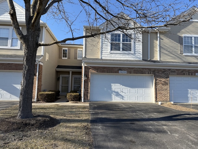 view of property with aphalt driveway, brick siding, and an attached garage