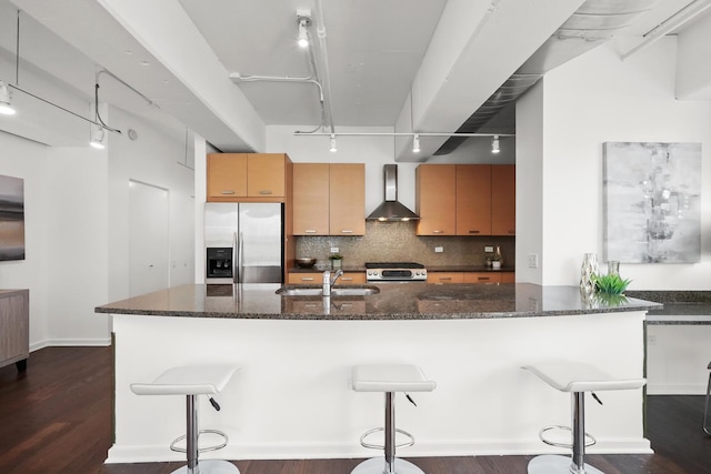 kitchen featuring tasteful backsplash, dark stone counters, appliances with stainless steel finishes, wall chimney exhaust hood, and a sink