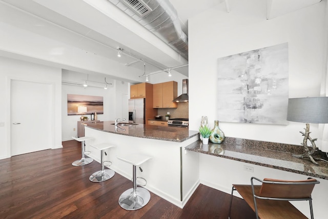 kitchen featuring dark wood-type flooring, wall chimney range hood, a breakfast bar area, appliances with stainless steel finishes, and a sink