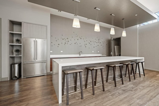 kitchen featuring a breakfast bar area, high end fridge, wood finished floors, and light countertops