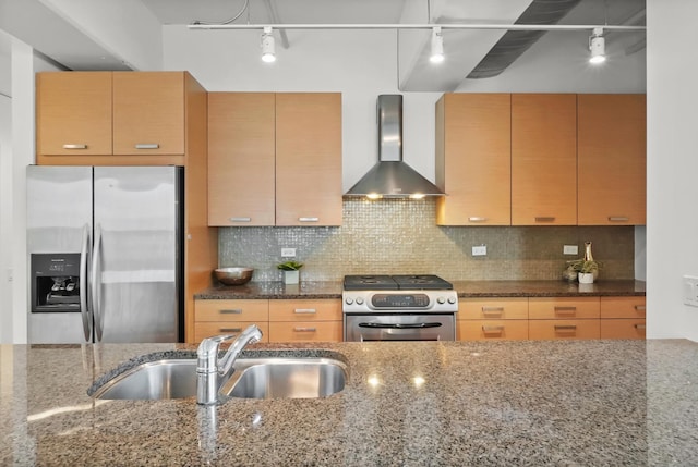 kitchen featuring dark stone countertops, a sink, stainless steel appliances, wall chimney exhaust hood, and backsplash