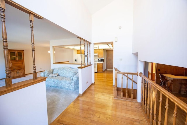 hall with a high ceiling, an upstairs landing, light wood-style floors, and baseboards