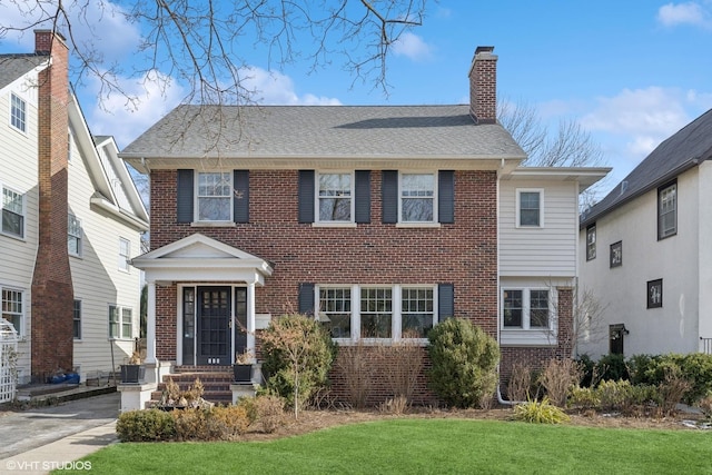 view of front of property featuring a front yard, brick siding, a chimney, and a shingled roof