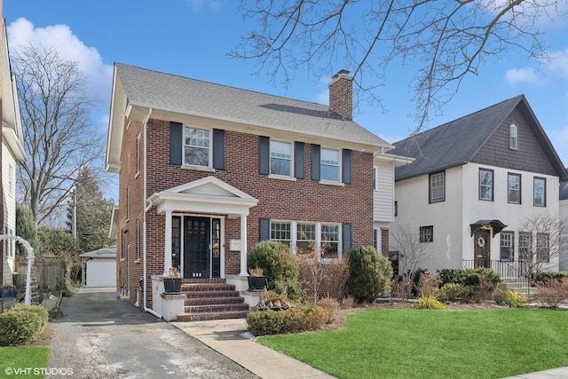 view of front of house with a front lawn, an outdoor structure, a garage, brick siding, and a chimney