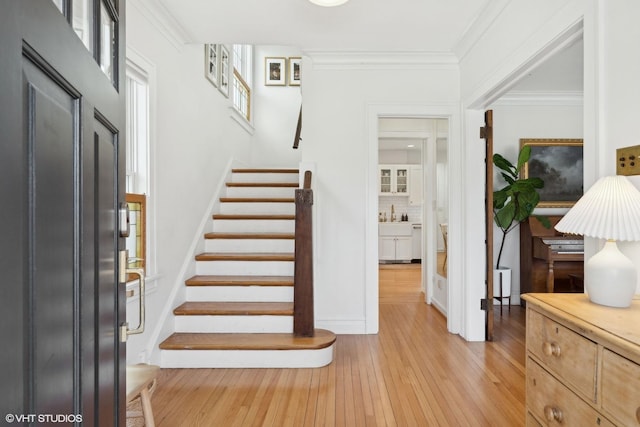 foyer entrance with crown molding, light wood-style flooring, plenty of natural light, and stairway