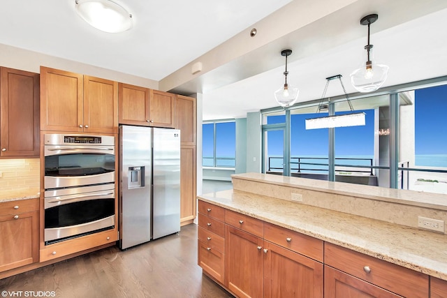 kitchen featuring light stone counters, appliances with stainless steel finishes, pendant lighting, and dark wood-type flooring