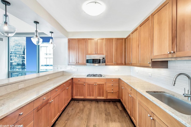 kitchen with light stone counters, wood finished floors, stainless steel appliances, a sink, and backsplash