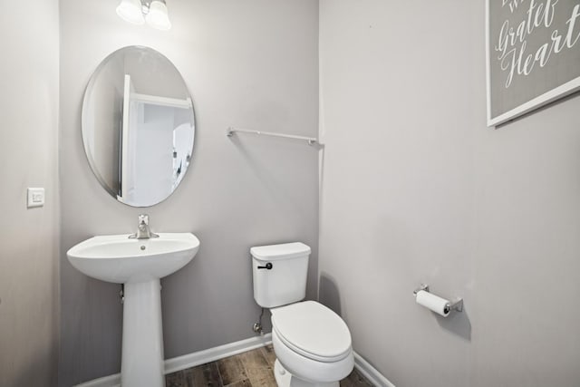 half bath with toilet, wood finished floors, baseboards, and a sink