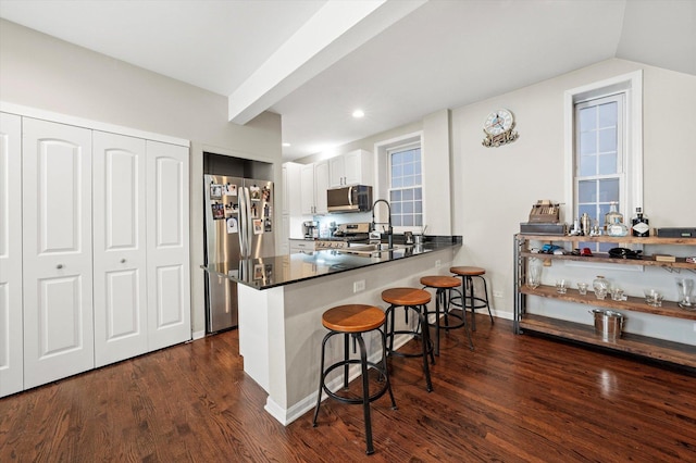 kitchen featuring white cabinetry, a peninsula, dark wood-style flooring, appliances with stainless steel finishes, and a kitchen bar