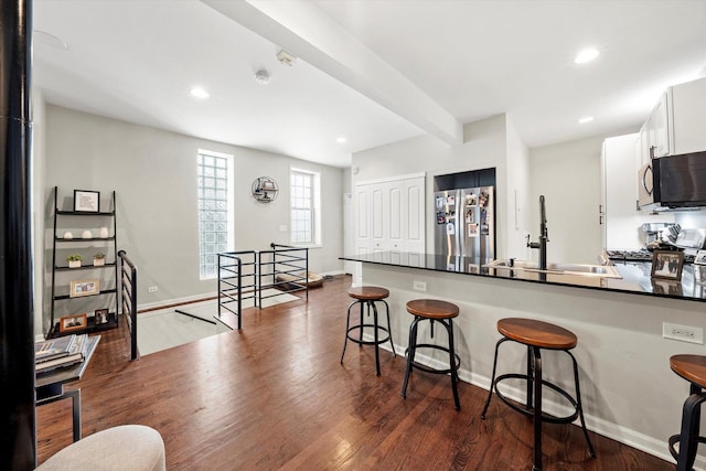 kitchen with dark countertops, beamed ceiling, a kitchen bar, freestanding refrigerator, and a sink