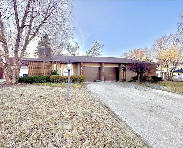 ranch-style home featuring aphalt driveway, a garage, brick siding, and a chimney