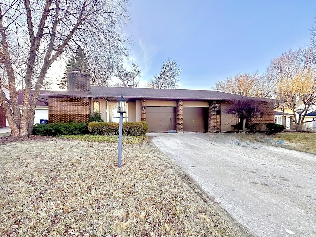 ranch-style house featuring brick siding, driveway, an attached garage, and a chimney