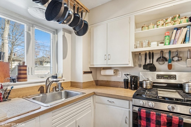 kitchen featuring a sink, open shelves, stainless steel gas stove, and white cabinetry