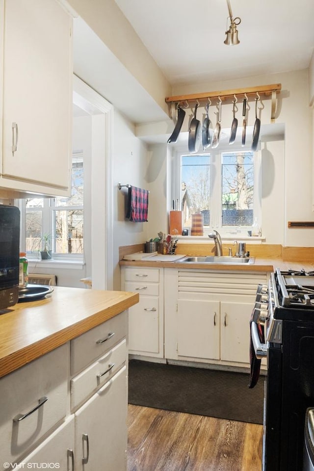 kitchen with wooden counters, range with gas stovetop, dark wood-style flooring, white cabinetry, and a sink