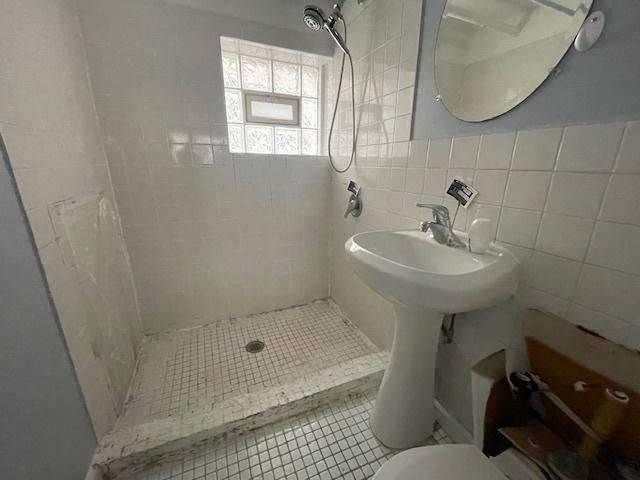 bathroom with tile walls, toilet, a stall shower, and tile patterned floors