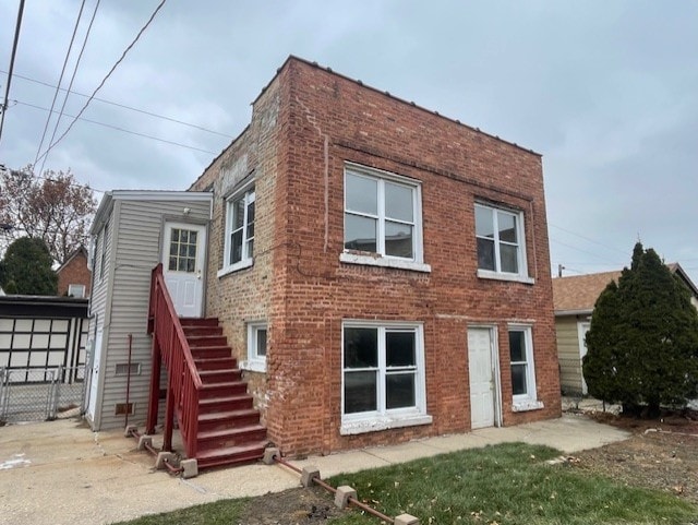 rear view of house with brick siding, stairs, and fence