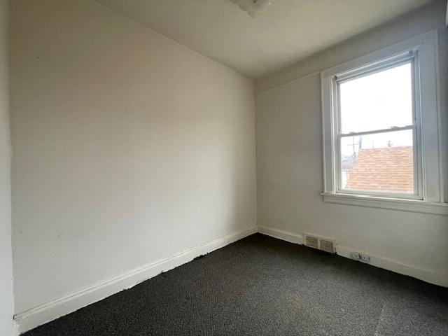 unfurnished room with visible vents, dark carpet, and baseboards