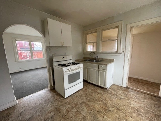 kitchen with baseboards, white gas range, white cabinets, arched walkways, and a sink