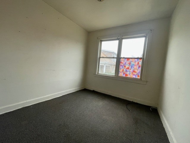 unfurnished room with dark carpet, baseboards, and vaulted ceiling