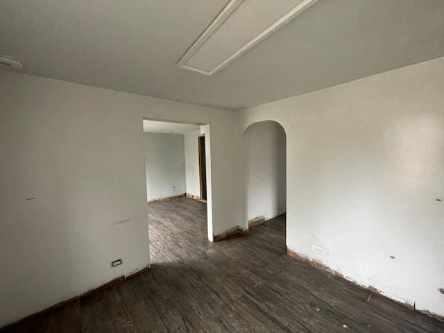 empty room with arched walkways, baseboards, attic access, and wood finished floors