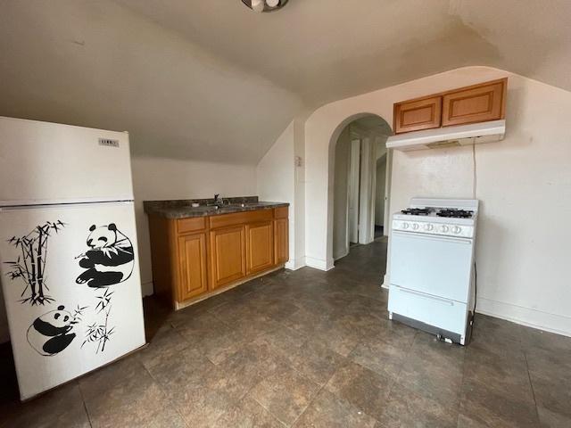 kitchen featuring under cabinet range hood, dark countertops, white appliances, arched walkways, and vaulted ceiling