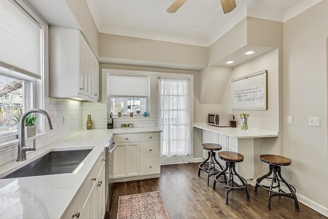 kitchen with a sink, tasteful backsplash, dark wood-style floors, appliances with stainless steel finishes, and light stone countertops