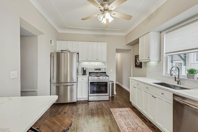 kitchen featuring light stone counters, a sink, stainless steel appliances, dark wood-type flooring, and white cabinetry