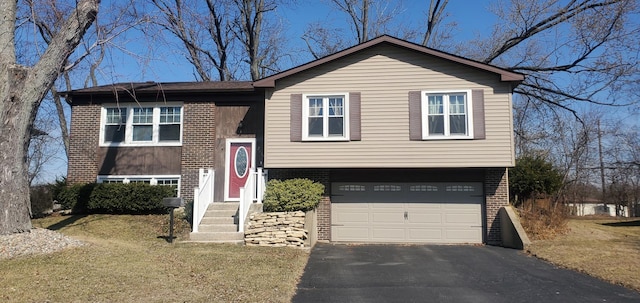 bi-level home featuring aphalt driveway, brick siding, a garage, and a front lawn