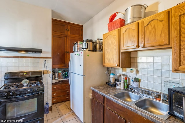 kitchen featuring gas stove, light tile patterned flooring, freestanding refrigerator, a sink, and under cabinet range hood